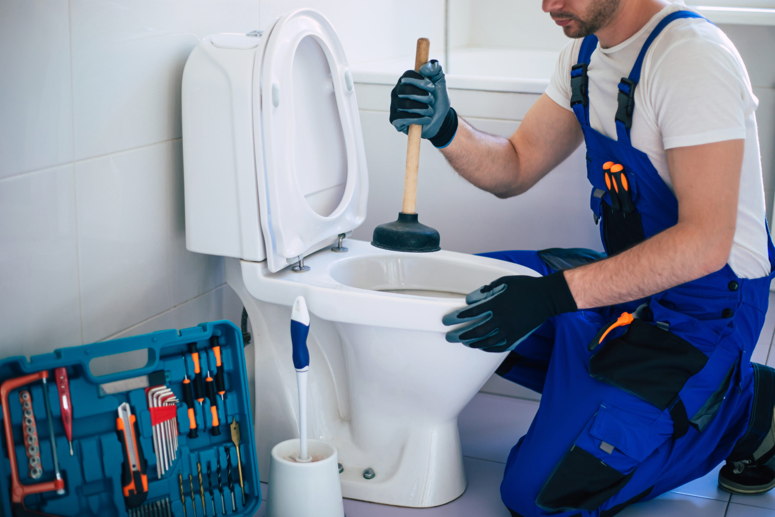 A plumber tightening the base bolts on a white residential toilet.